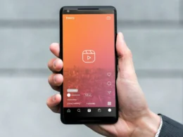 A hand holding a smartphone showing the reels interface of a social media app with a gradient background.